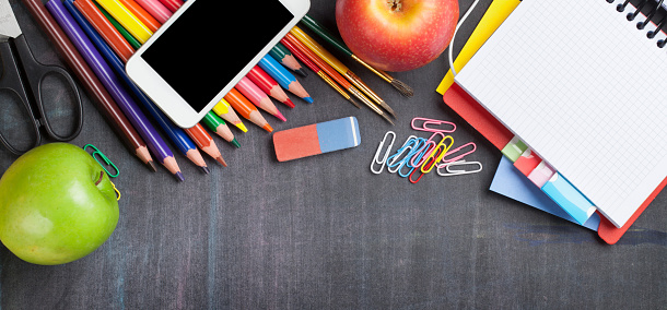 School and office supplies on blackboard background. Top view with copy space. Wide flat lay
