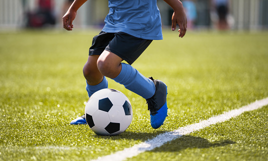 African American young boy playing soccer in a stadium pitch. Child running with soccer ball along the field white sideline. Junior soccer background
