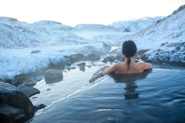 Photo of The girl bathes in a hot spring in the open air with a gorgeous view of the snowy mountains. Incredible iceland in winter