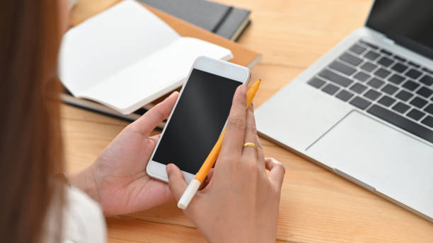 istock Close-up image of young creative woman while holding/using a black blank smartphone on the working desk. 1199904013