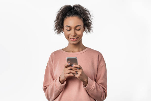 istock Happy young afro american woman using mobile phone while standing isolated over white background 1199905244
