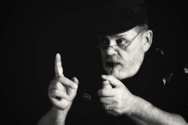 artistic low key portrait of bearded senior man holding tobacco pipe and pointing forefinger up in darkness - portrait black and white senior men wisdom imagens e fotografias de stock