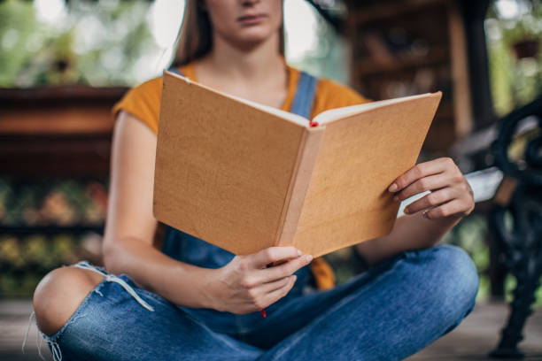 istock Young woman reading a book on a porch 1199910574