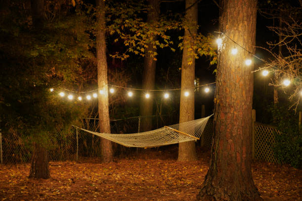 eine hängematte wird zwischen zwei bäumen in einem hinterhof mit café-lichter aufgehängt; romantische nächtliche einstellung; landschaftsansicht - strung stock-fotos und bilder