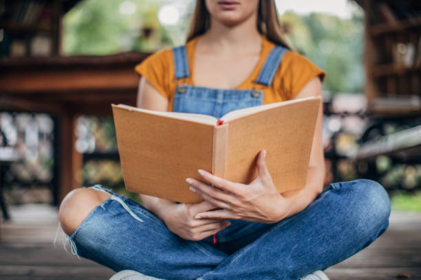 istock Young woman reading a book on a porch 1199910943