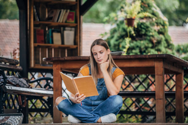 istock Young woman reading a book on a porch 1199911073
