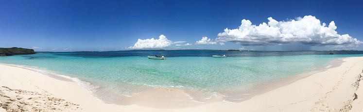Panorama of two boats anchored to turquoise waters off a white sand beach under a blue sky in Abaco, Bahamas; landscape