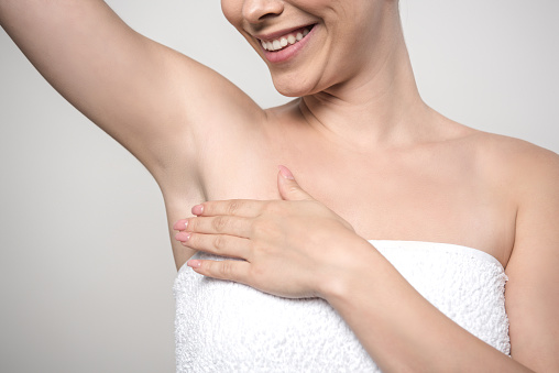 cropped view of smiling woman touching underarm isolated on grey