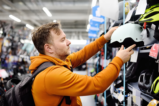 Middle age man choosing and trying on bicycle helmet in sport store. Healthy active style of life.