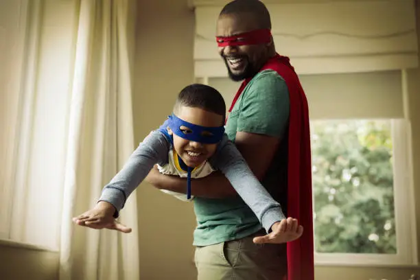 Smiling son and father pretending to be a superhero at home