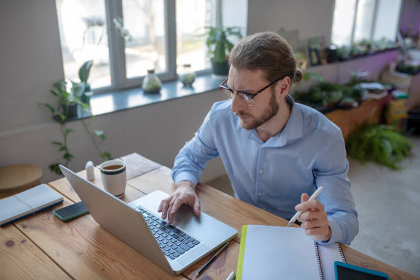 istock Young man in glasses, working at laptop, taking notes in notebook. 1199935272