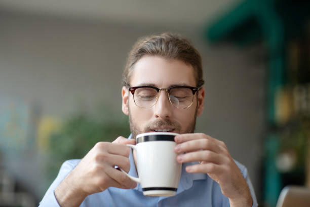 istock Young man with glasses looking smiling at a cup of coffee. 1199935298