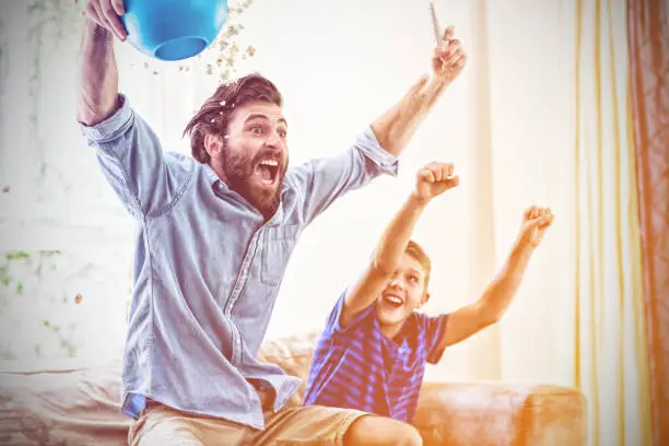 Photo of Excited father and son watching television