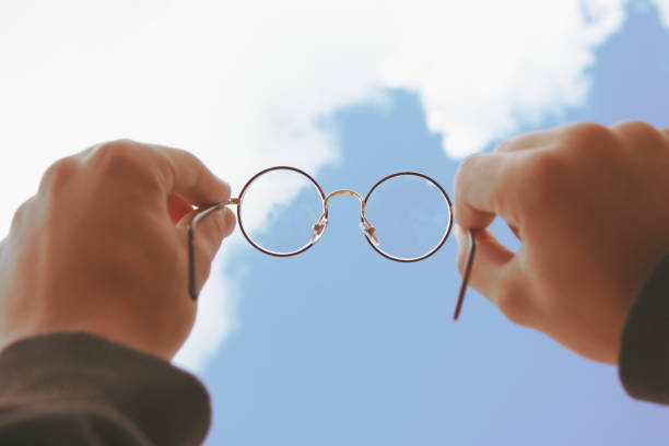 istock Two hands holding round frame glasses looking upwards to the sky 1199943787