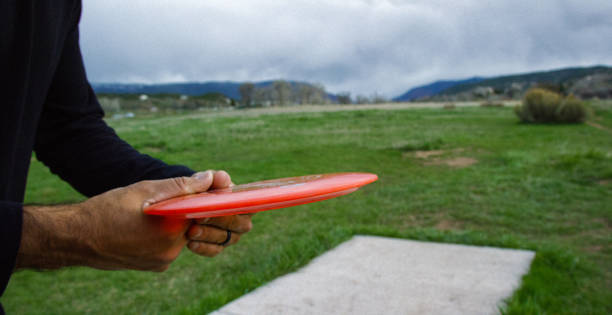close-up of man preparing to throw a disc golf driver a long distance across an outdoor area with trees under storm clouds - golf expertise professional sport men imagens e fotografias de stock