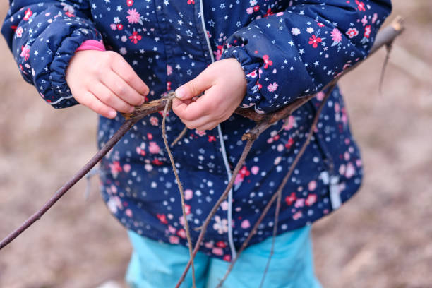 Caucasian child girl in warm winter clothing playing with twig and string stock photo