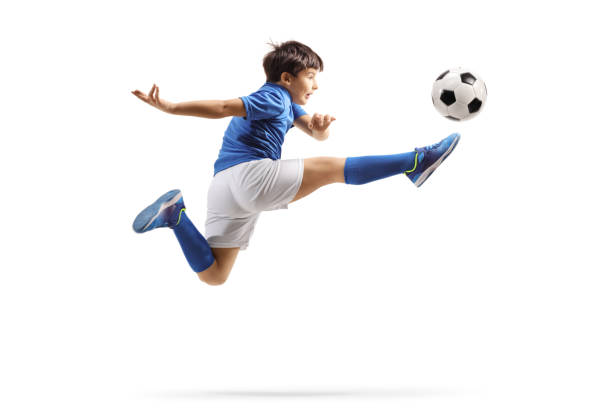 ragazzo in una maglia sportiva saltando e calciando un pallone da calcio - soccer child indoors little boys foto e immagini stock