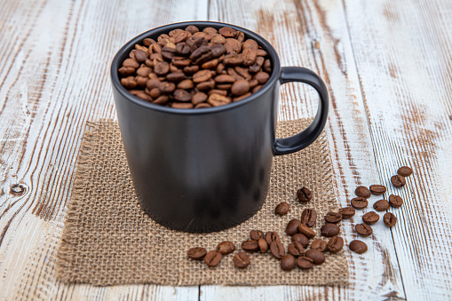 Coffee cup, filled with coffee beans. Coffee beans in a cup on wooden background.