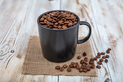 Coffee cup, filled with coffee beans. Coffee beans in a cup on wooden background.