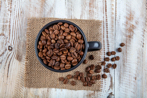 Coffee cup, filled with coffee beans. Coffee beans in a cup on wooden background.