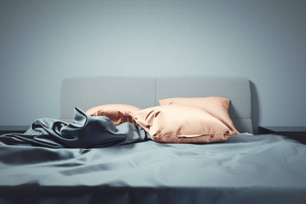 istock Unmade bed with soft clean satin linen and pillows. 1199961365