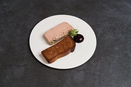 Toasted bread with pate in white plate on dark background with copy space, close-up. Chicken liver pate with blackcurrant and fig sauce