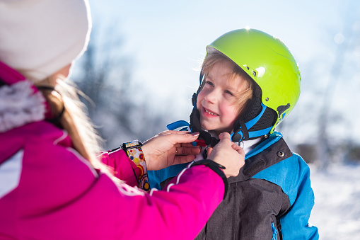 Mother helps her son to put on a ski helmet