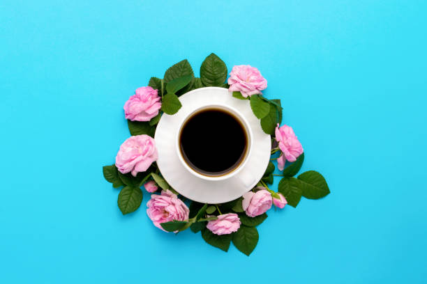 istock White cup with black coffee and pink roses lined around on a blu 1199962037