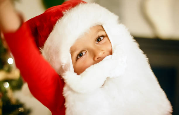istock A Five Year-Old Caucasian Boy Tilts His Head to the Side while Wearing a Santa Hat and Beard in Front of a Christmas Tree 1199967995