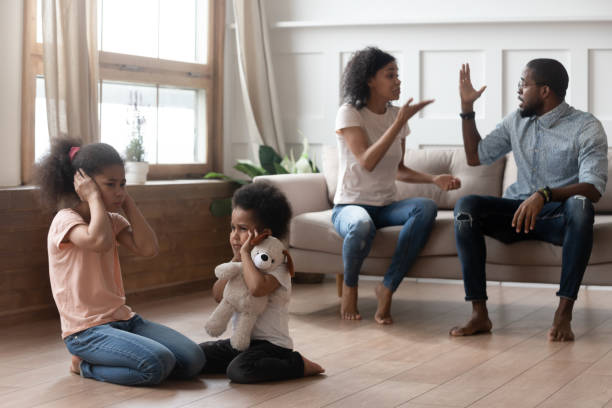 Upset children suffering from parent family conflicts. African american angry married couple arguing and shouting, while two mixed race upset stressed kids sitting on floor, closing ears hurt by parents fighting, family conflicts, divorce concept. man closing ears photos stock pictures, royalty-free photos & images