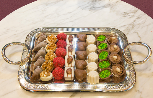 Beautiful variety of tasty chocolates dessert on a silver vintage tray for special occasions, Valentine and Christmas. Stylish arrangement sweet. Marble texture background. Horizontal close-up.