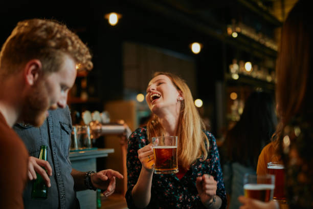 un piccolo gruppo di migliori amici in piedi in un pub, bevendo birra, chiacchierando e divertendosi. concentrati sul barista che pulisa il bicchiere da bere. vita notturna. - irish culture beer drinking pub foto e immagini stock