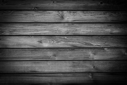 A full frame abstract background of a black and white monochrome knotted wood grain plank wall background with a rustic retro style and a dark vignette.