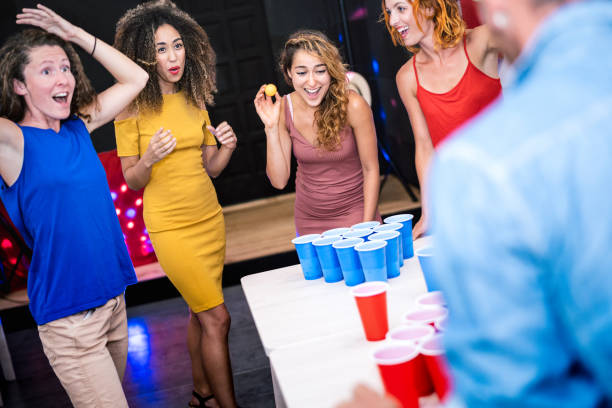 glückliche freunde gruppe spielen bier pong in jugendherberge - reise und spaß konzept mit backpackern mit echtem spaß zusammen im gästehaus spielzimmer - lebendige farbfilter mit fokus mädchen werfen ball - trinkspiel brettspiel stock-fotos und bilder