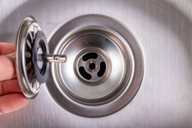 Drain in the metal kitchen sink. Drainage installation in a home kitchen. Light background.
