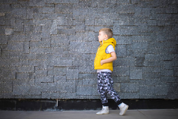 istock Side view of a kid walking by the brick wall. 1199982867