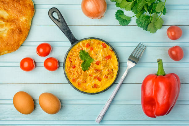 istock On a blue background, a pan with a Turkish national recipe. Omelet made from eggs, tomato, onion and pepper, Menemen. Flat lay. 1199985528