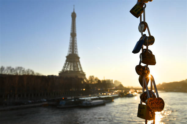 Paris, France-12 30 2019:Group of padlocks hung by lovers hanging in front of the Seine river and the silhouette of the Eiffel tower in Paris, France.