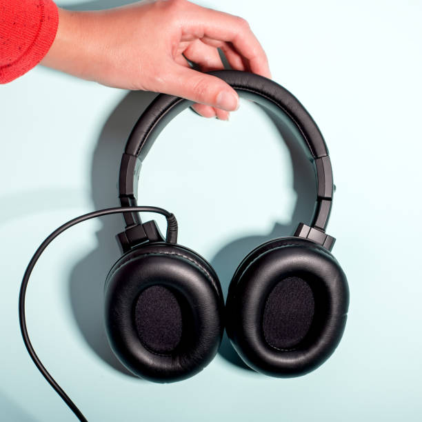 istock Black massive headphones in female hand on pastel background, copy space. Modern technology flat lay with over-ear earphones in woman hand, modern lifestyle concept 1199988520