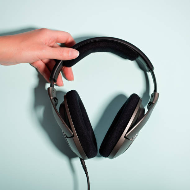 istock Black massive headphones in female hand on pastel background, copy space. Modern technology flat lay with over-ear earphones in woman hand, modern lifestyle concept 1199988521
