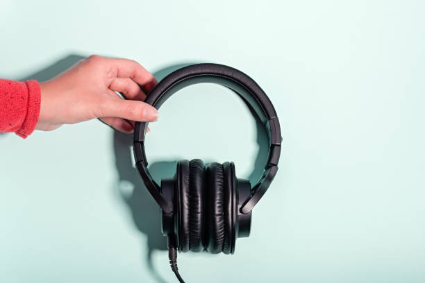 istock Black massive headphones in female hand on pastel background, copy space. Modern technology flat lay with over-ear earphones in woman hand, modern lifestyle concept 1199988524