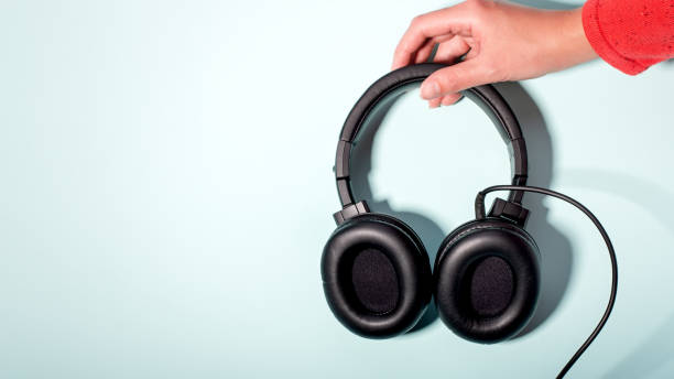 istock Black massive headphones in female hand on pastel background, copy space. Modern technology flat lay with over-ear earphones in woman hand, modern lifestyle concept 1199988525