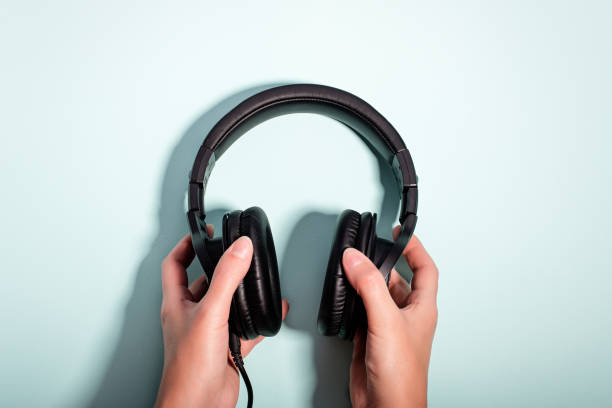 istock Black massive headphones in female hand on pastel background, copy space. Modern technology flat lay with over-ear earphones in woman hand, modern lifestyle concept 1199988528