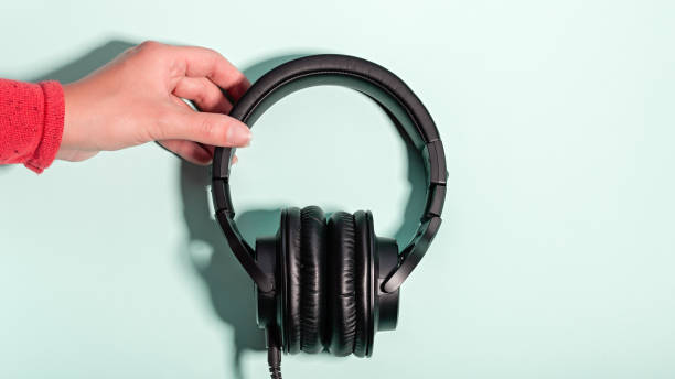 istock Black massive headphones in female hand on pastel background, copy space. Modern technology flat lay with over-ear earphones in woman hand, modern lifestyle concept 1199988529