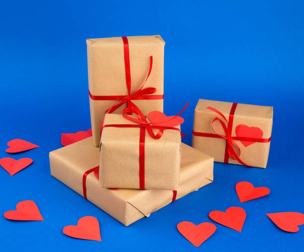 istock rectangular box is wrapped in brown paper and tied with a red thin silk ribbon on a blue background, red cut out paper hearts 1199990362
