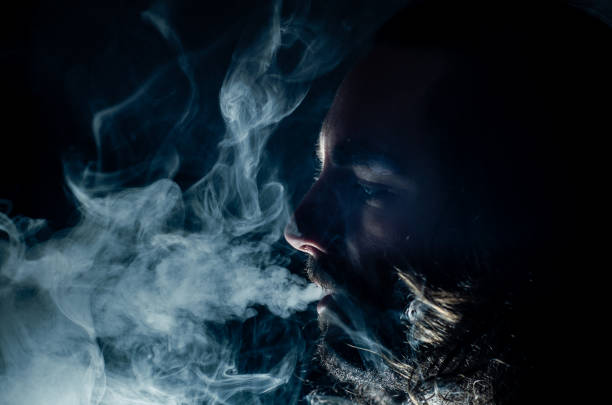 hombre fumador exhalando mucho humo de vapeo, con espacio de copia. - low key lighting flash fotografías e imágenes de stock