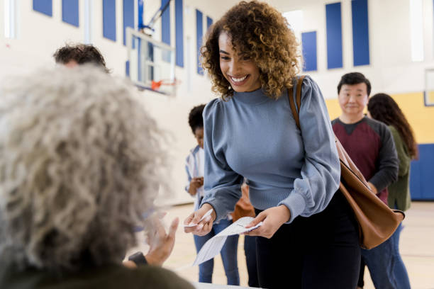 istock Woman smiles while handing volunteer her information for voting 1199991173