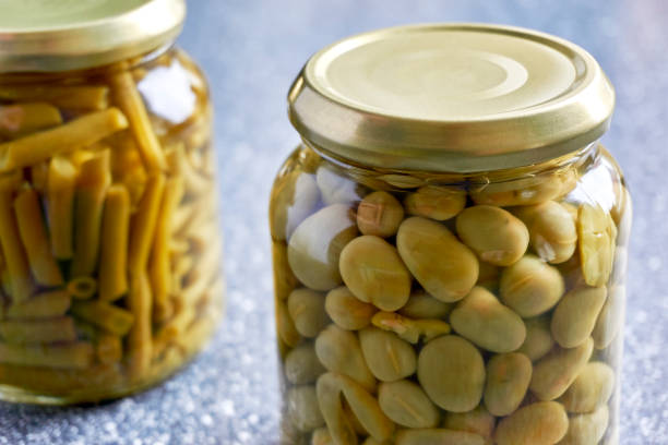 Closeup of two glass jars with canned broad beans and green beans on kitchen top. Image with selective focus.