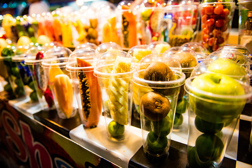 In Phuket, Thailand a night market vendor displays and sells a variety of fresh fruit from plastic cups.