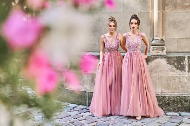 Beautiful bridesmaids in gorgeous elegant stylish red pink violet floor length v neck chiffon gown dress decorated with sequins sparkles and rhinestones holding flowers bouquets. Wedding day in old beautiful European city. hermosas damas de honor en precioso elegante elegante rosa rosa violeta largo del piso v cuello vestido de novia decorado con lentejuelas destellos y pedrería sosteniendo ramos de flores. día de la boda en la vieja y hermosa ciudad europea. copiar espaci